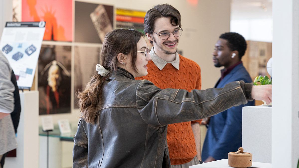 college students looking at and pointing to a piece of artwork in a gallery.