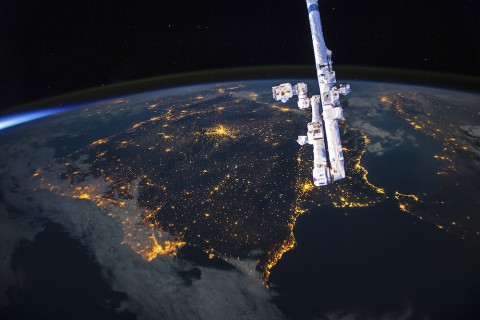 View of clustered tiny city lights on earth from space station with solid black sky.