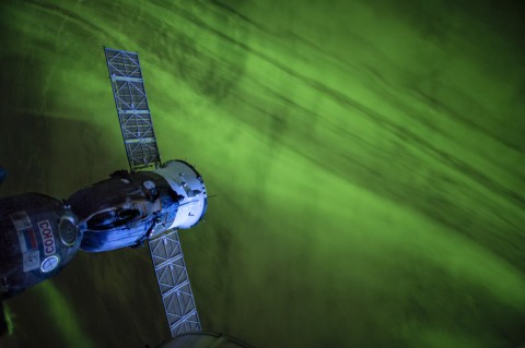 Image of Space Station flying above a river of green aurora.