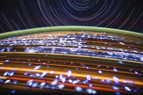 Blurred image of star trails in multi colors across a gentle arch of the earth's curvature highlighted with a green stripe.