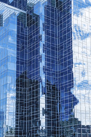 Manipulated and abstracted photographic image of glass walled sky scraper in blues and reflects clouds