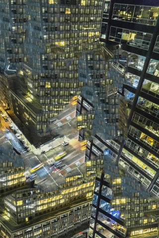 Manipulated and abstracted photographic image of night scene of city glass walled skyscrapers looking down into the street with traffic and blurred headlights