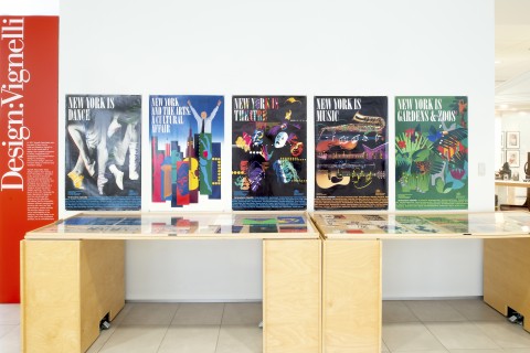 View of five posters mounted on a wall above a large glass top table.