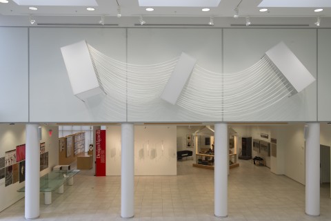 View of exhibition wall with three 3D rectangular forms mounted on the wall with series of cords draped between.