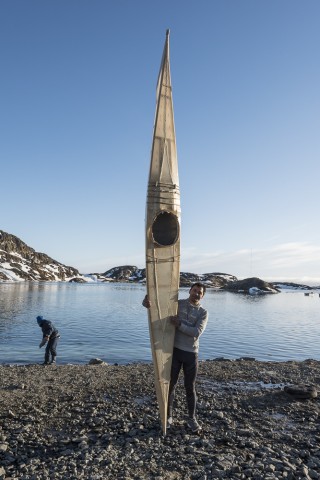 Man standing at ocean's edge holding a single man kayak upright.