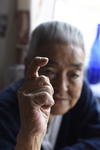 Elderly grey haired woman holding her hand with a crooked finger in front of her face.