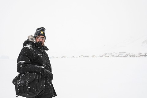 Man wearing a full arctic winter suit while standing in snowy arctic landscape.