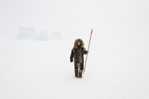 Woman wearing full seal skin suit holding a long spear while standing in winter landscape