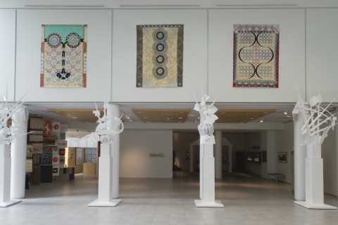 View of gallery installation - one wall with three large painted canvases that resemble oriental carpets above ground level arcade area.