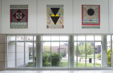 View of gallery installation - one wall with three large painted canvases that resemble oriental carpets above ground level plate glass windows.