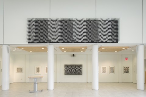 View of gallery installation - one wall with large horizontal black and white wall hanging on upper level above lower arcade with undulating pattern.