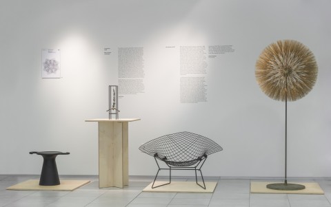 Image of four objects - a modern black round table, a metal cage form with a suspended abstract human form, a wire mesh chair, a metal dandelion-gone-to-seed metal sculpture. 