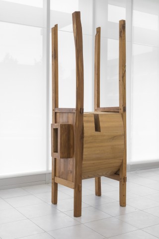 Floor standing vertical sculpture with four long thin wood supports with wooden assemblage of wood blocks in the center. 