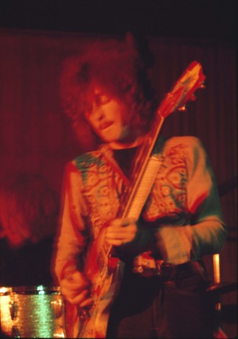 Color photo portrait of musician Eric Clapton, blurred in motion while standing and playing the electric guitar. 