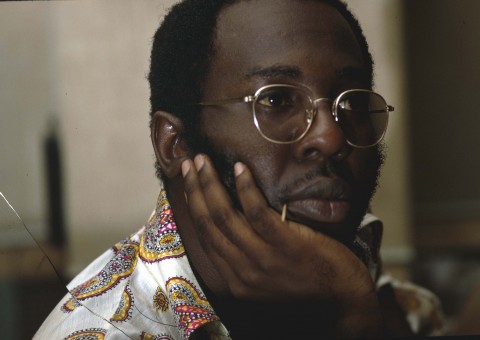 Color photo portrait of musician Curtis Mayfield wearing wire rimmed glasses cradling his chin in his right hand.