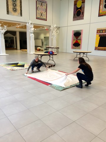 Artist and assistant with one large painting on the floor prepping it to be rolled in a sheet after exhibition.