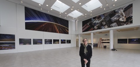 Image of woman standing in gallery with two 30 foot photo murals mounted on the second level of the walls.