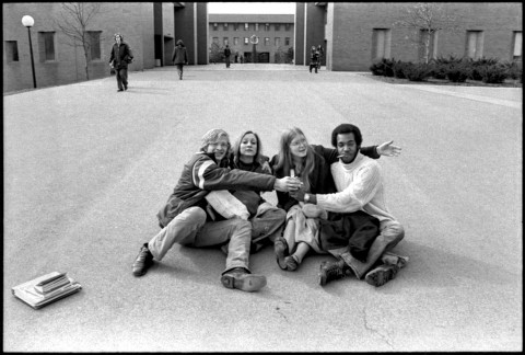Four students sitting in the middle of a walkway with their arms around each other