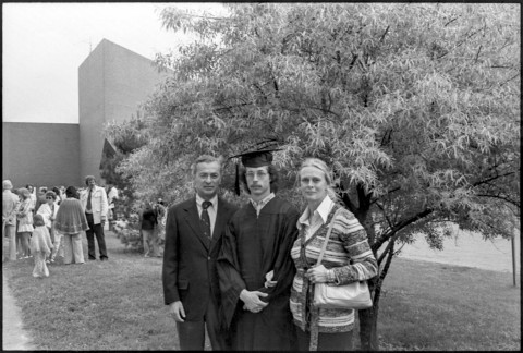 Family group of two patterns standing with their son who is wearing a graduation robe and cap
