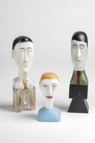 A trio of wooden carved male heads with serious expressions, painted hair and glass bead eyes