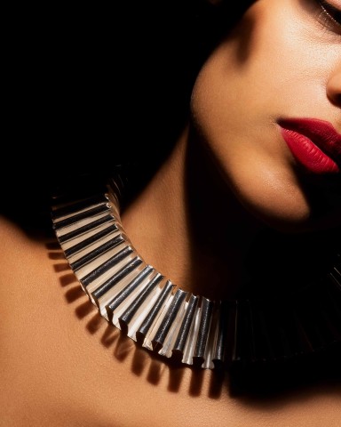 Close up of woman's face that leans to right with sculptural necklace around neck