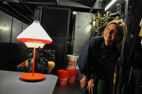 a person looking at a lamp with a red metal base and a white glass shade.