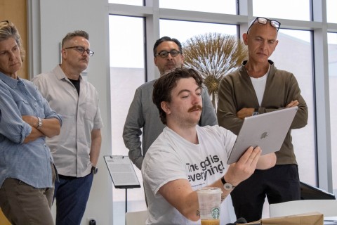 a group of people gathered around a person holding up an i-pad.