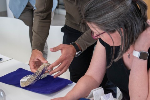 a person leaning on a table surface watching the hands of another individual arranging an object.