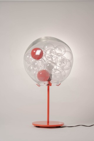 a lamp with a red metal base and glass shade against a grey background.