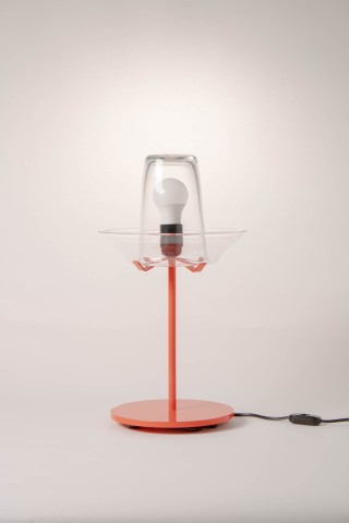 a lamp with a red metal base and glass shade against a grey background.