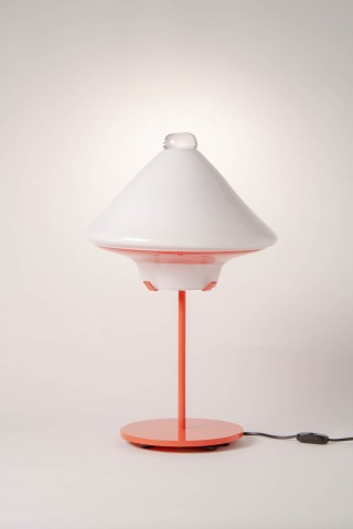 a lamp with a red metal base and glass shade against a grey background.