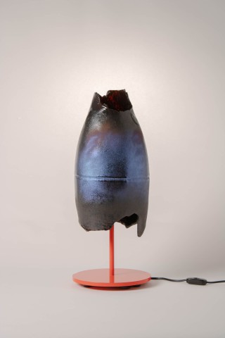 a lamp with a red metal base and glass shade against a grey background.
