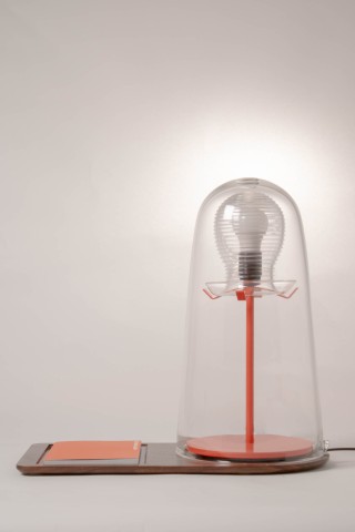 a lamp with a red metal base and glass shade against a grey background.