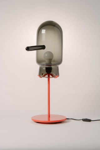 a lamp with a red metal base and glass shade against a grey background.