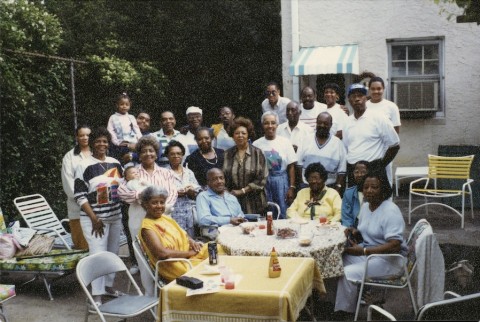 a faded color photograph of a large gathering of people around a table at a family re-union.