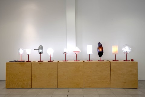 a view into the Grid Space gallery with a view of the display of lamps on wood stands.