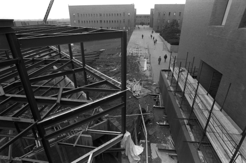a black and white aerial photograph with a view of a steel structure of a college building and walkway under construction.