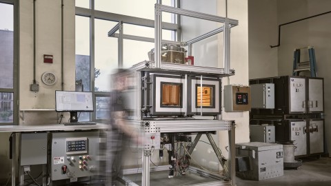 a view of a large metal kiln in a glass blowing studio with a glow of molten glass form inside.