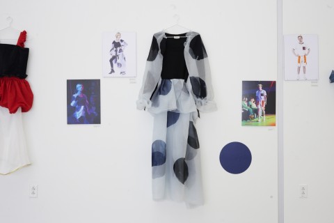 a line up of color photographs and costumes hung on a white gallery wall. 