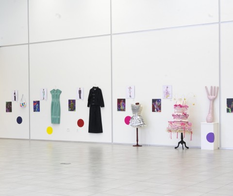 a line up of color photographs and costumes hung on a two-story white gallery wall.