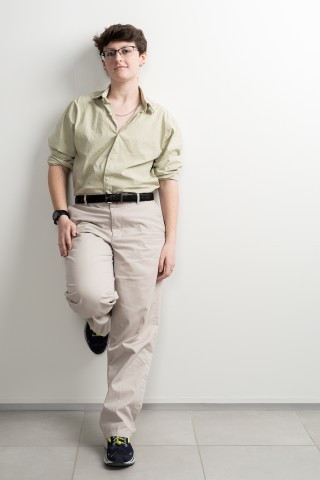 a color photograph of a person wearing a light green shirt and khaki pants leaning against a wall with one leg propped up on the wall.