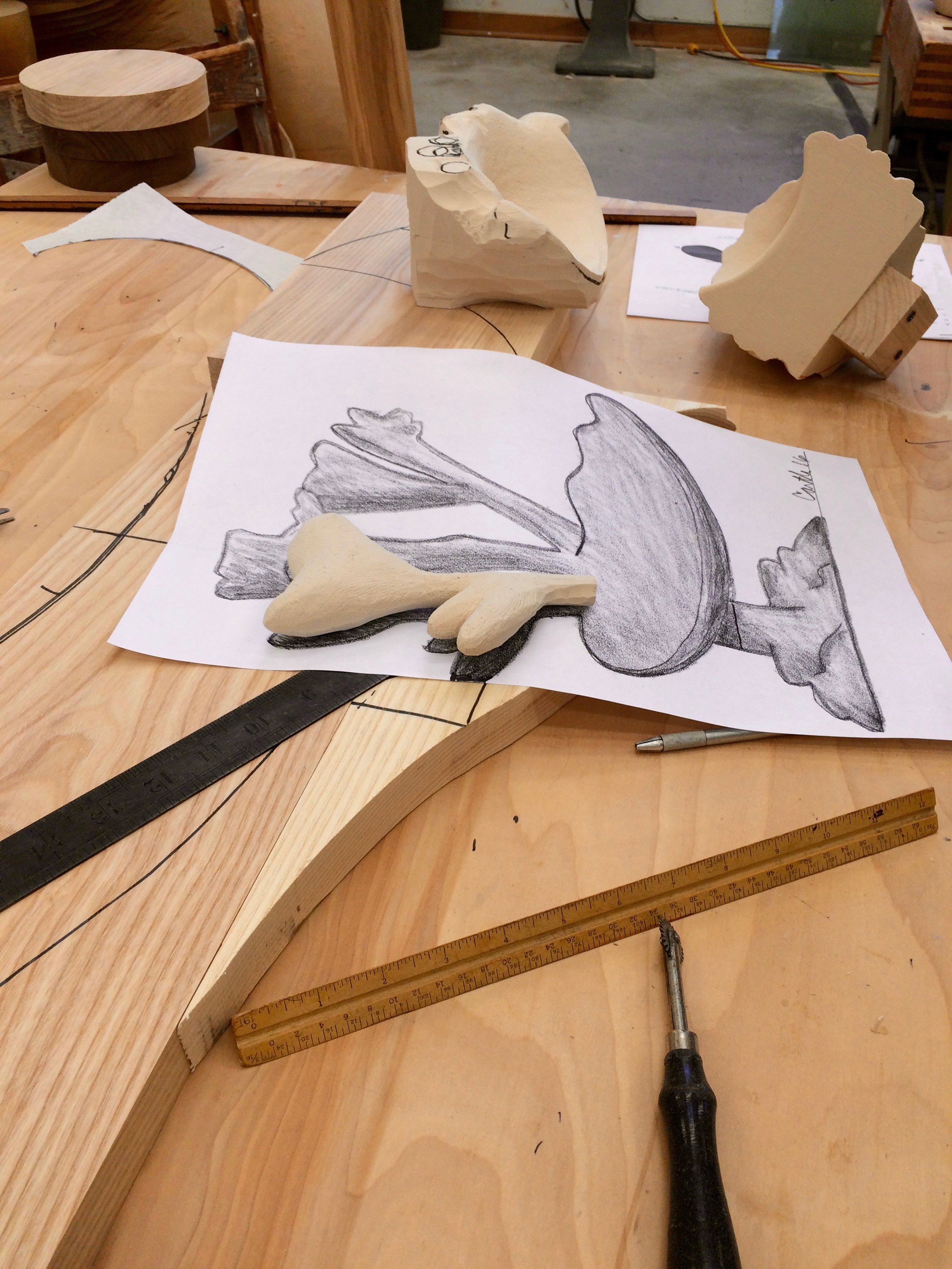 Image of a table top work space, a pencil drawing, wood chisels, and blocks of wood.