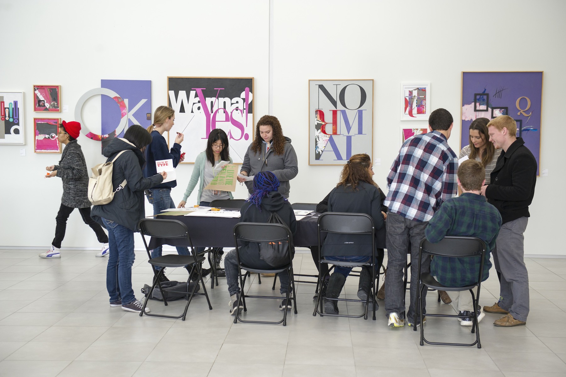 Group of students gathered around a table with graphic poster exhibition on walls in backdrop.
