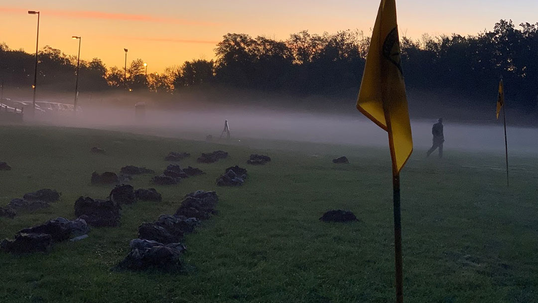 A flag in the foreground of a foggy field.
