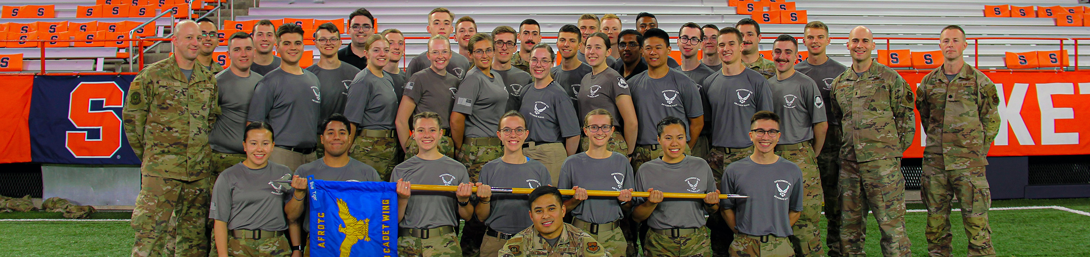 AF ROTC members posing in a stadium, holding a blue flag.