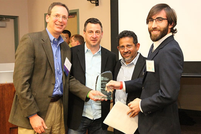 four people holding award together.