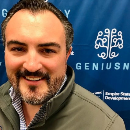 Head-and-shoulders view of man posing in front of blue banner