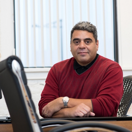 Man wearing red sweater sits at desk.