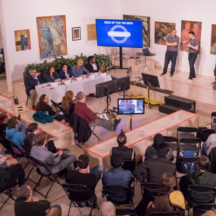 Overhead view of sitting crowd listening to presenters.