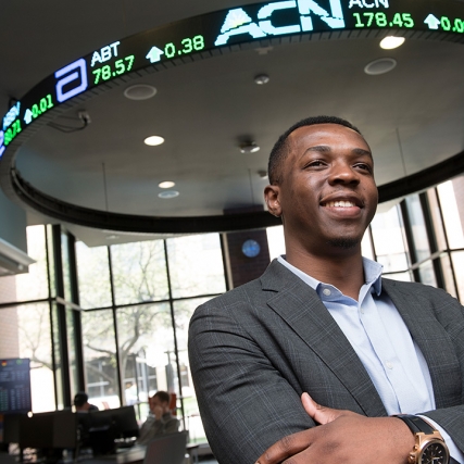Student poses below stock ticker sign.